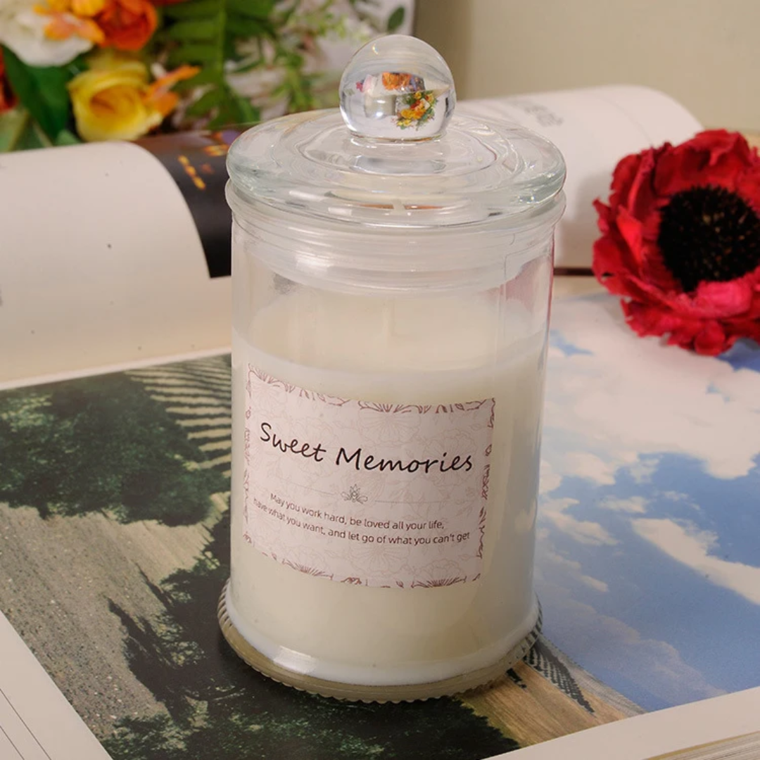 Candle in a glass jar labeled 'Sweet Memories' on a scenic background with flowers.