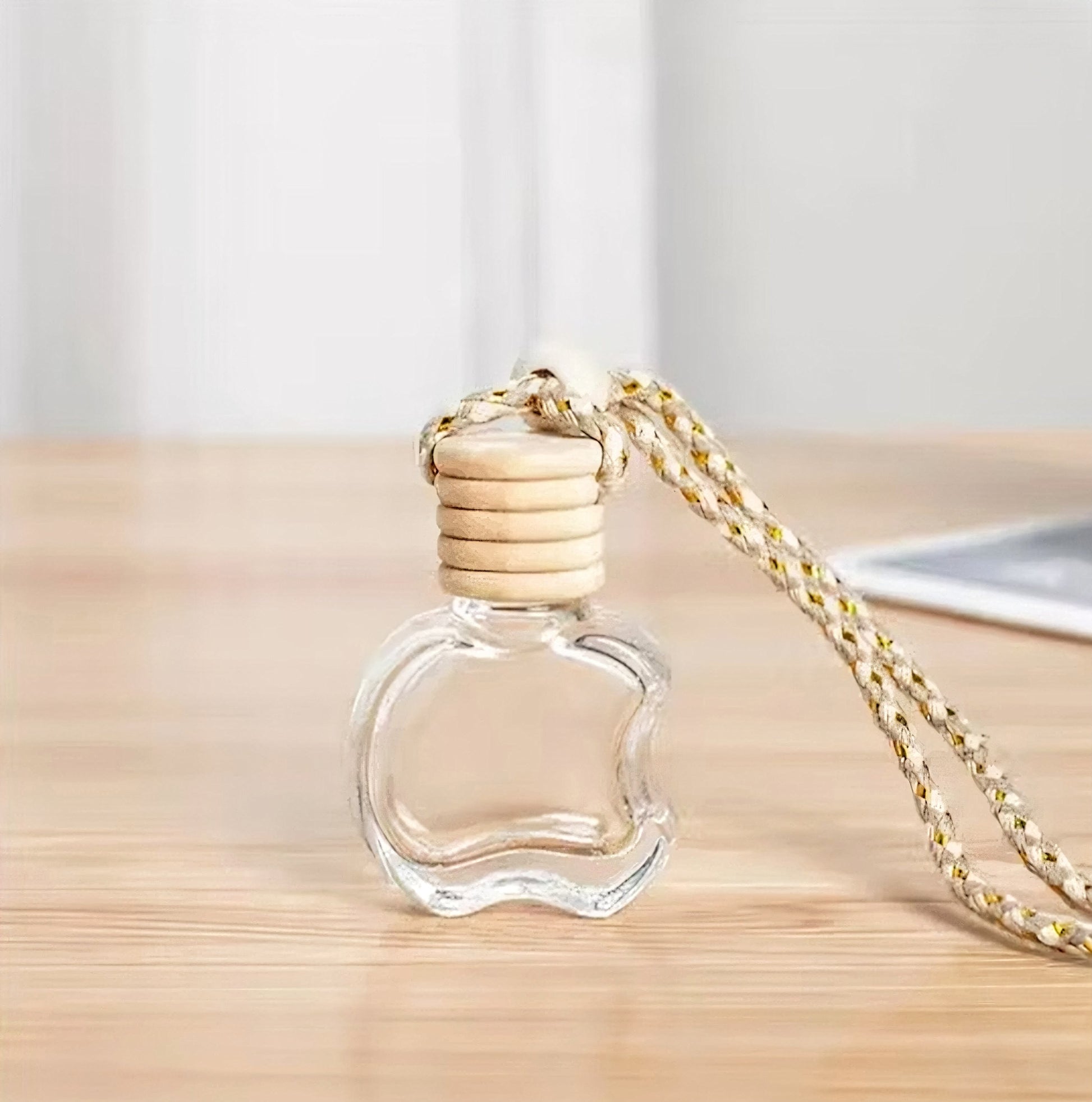 Clear glass perfume bottle with gold cap and chain on a wooden surface